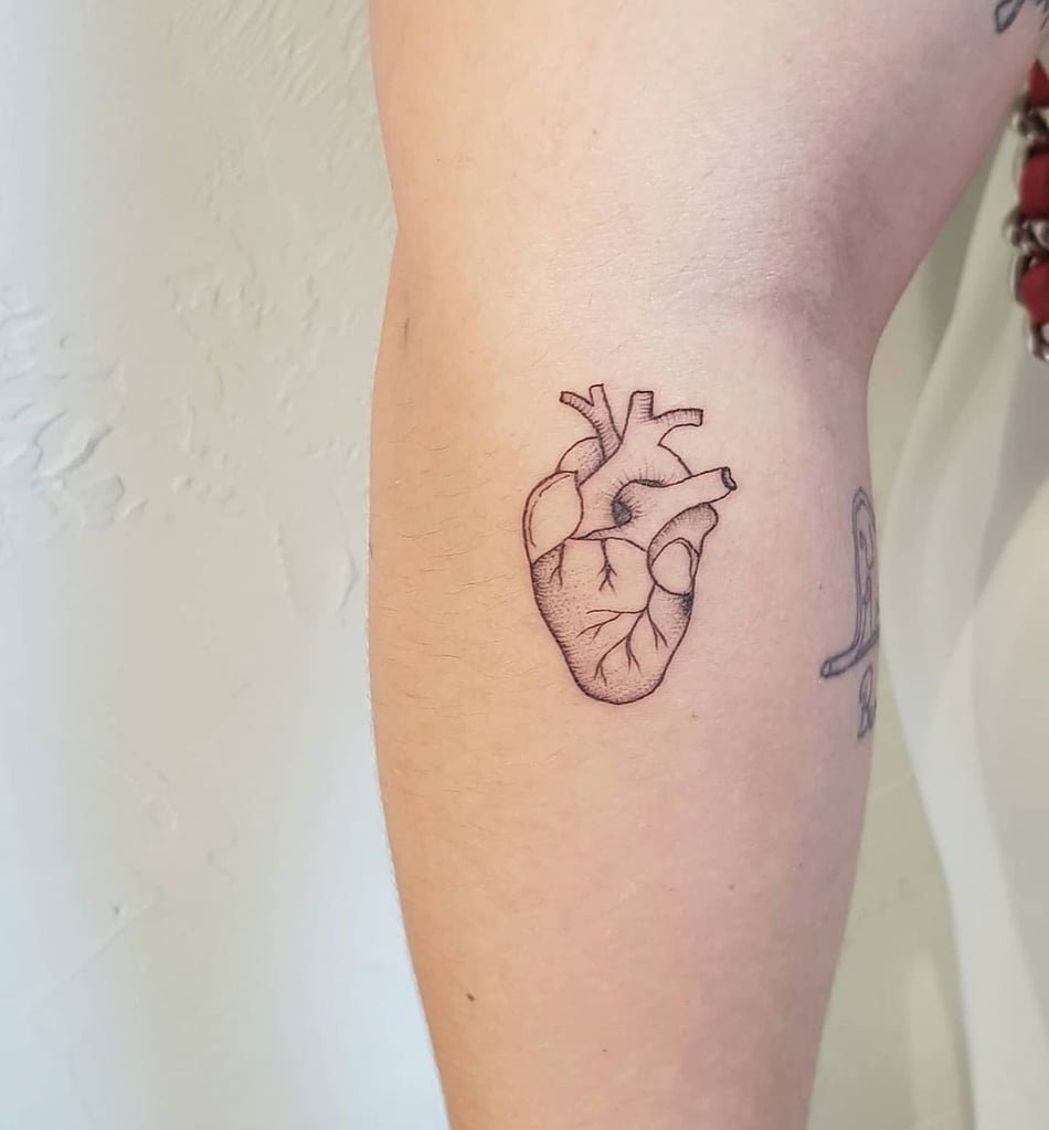 w950-1 Braço com tatuagem de coração anatômico em traços finos, próximo a outra tatuagem menor e indefinida.
