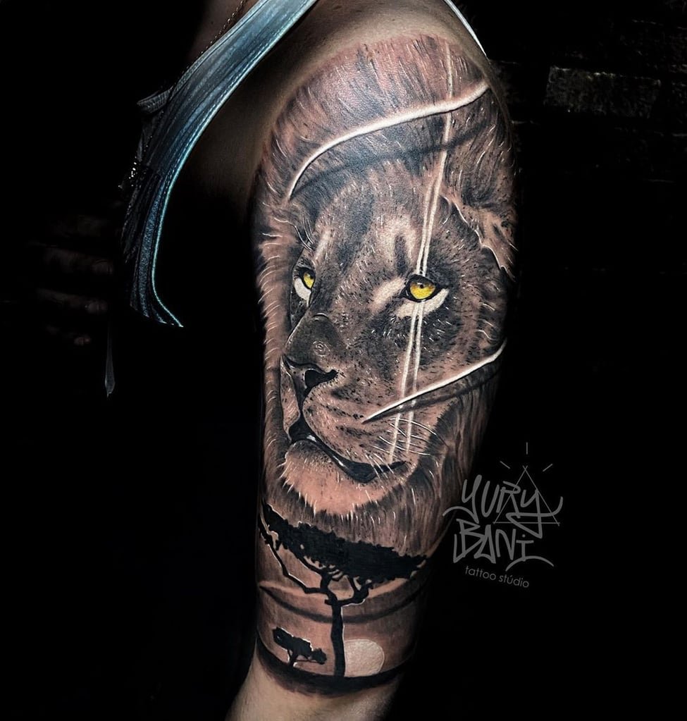 w975 Uma tatuagem detalhada de leão no braço, com paisagem de savana ao fundo.