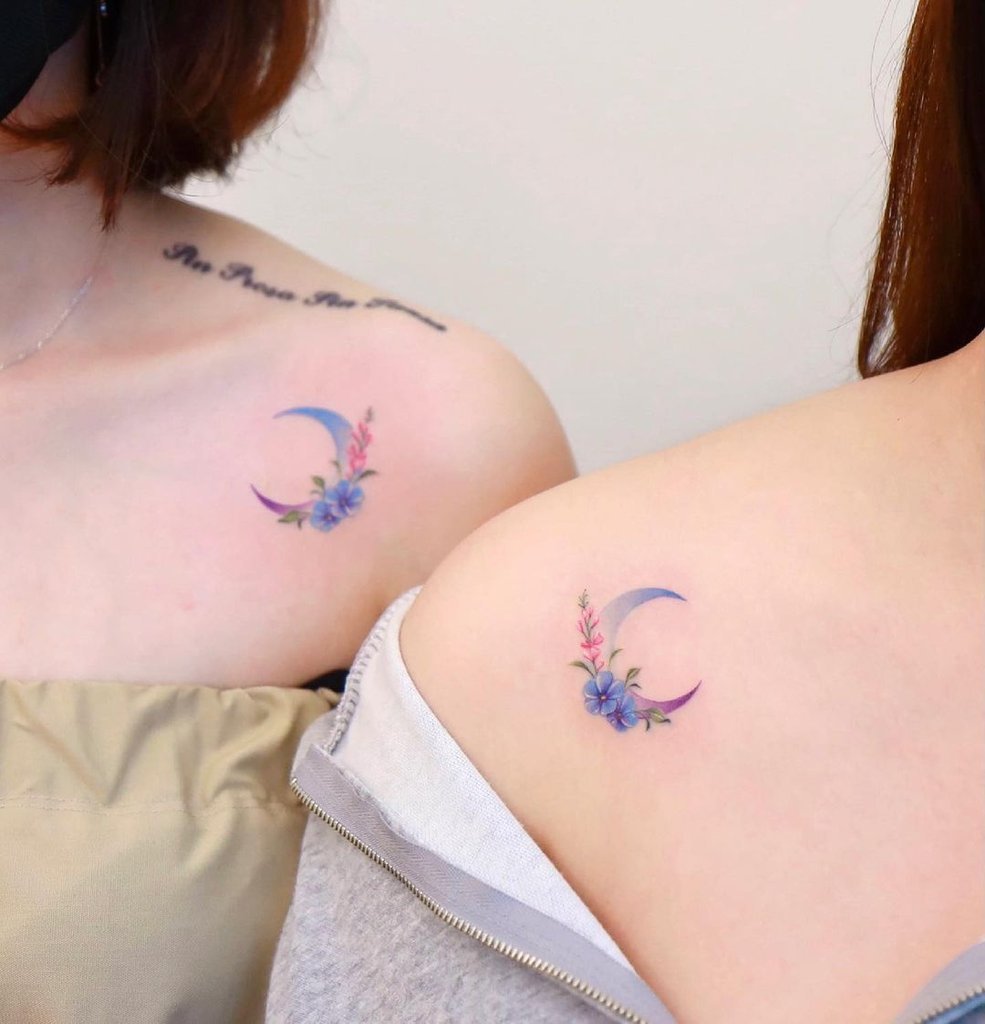 w985-3 Duas pessoas com tatuagens idênticas de lua e flores nos ombros, destacando-se pela cor vibrante e delicada.