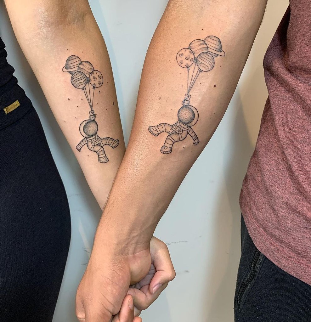 w988-3 Dois antebraços com tatuagens de astronautas segurando balões em formato de planetas.