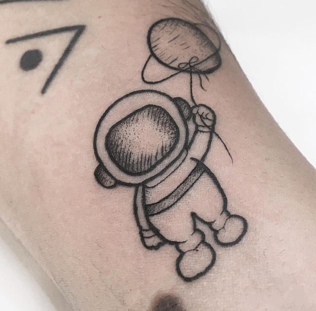 w9999-11 Tatuagem de astronauta segurando balão em forma de planeta, com linhas simples e minimalistas no braço.
