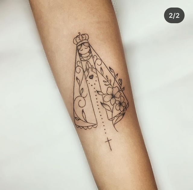 w9999-12 Uma tatuagem em um braço mostra uma figura com manto e flores, acompanhada de um rosário com uma cruz.