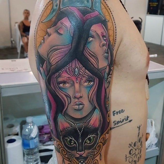 w9999-6 Tatuagem colorida no braço com rostos femininos interligados e um gato na parte inferior.