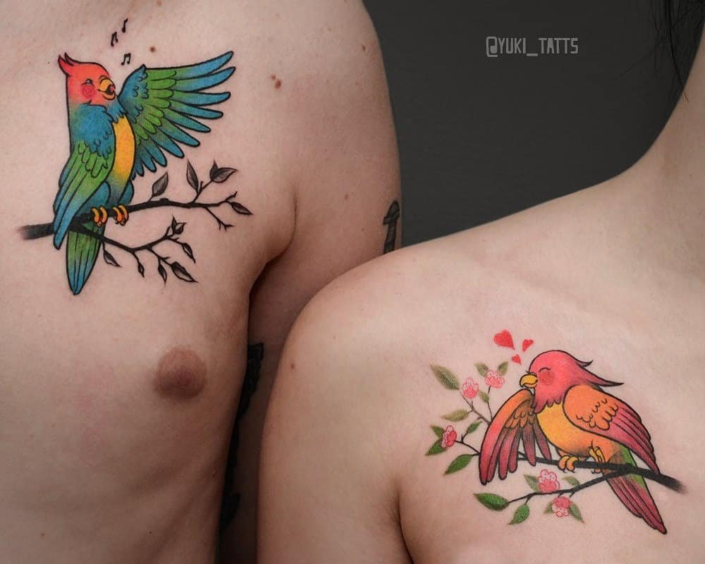 w9999-63 Duas tatuagens de pássaros coloridos em ramos, uma com notas musicais e outra com corações, no peito de duas pessoas.