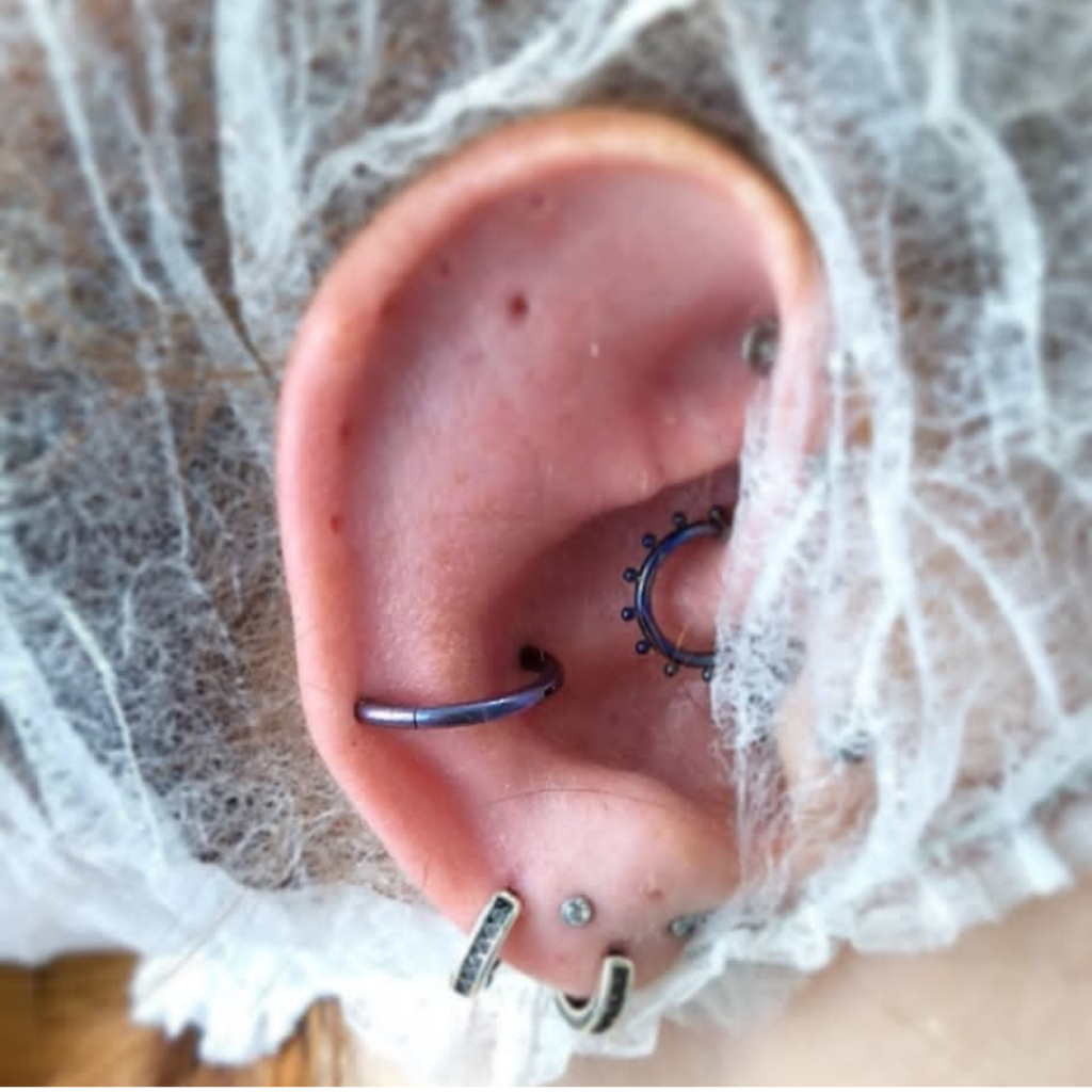 Close-up de orelha com piercings diferenciados em ambiente de estúdio profissional para perfuração.