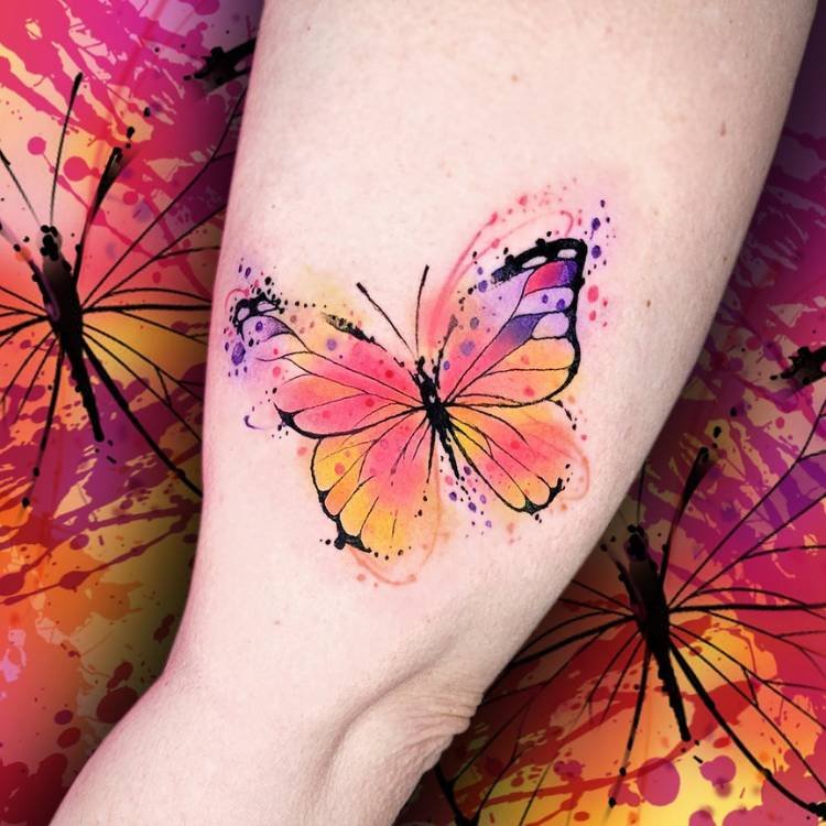aquarela-rosa-amarelo-roxo-borboleta Tatuagem de uma borboleta em estilo aquarela com as cores roxo, rosa e amarelo. Ela está feita no braço de uma mulher de pele clara.