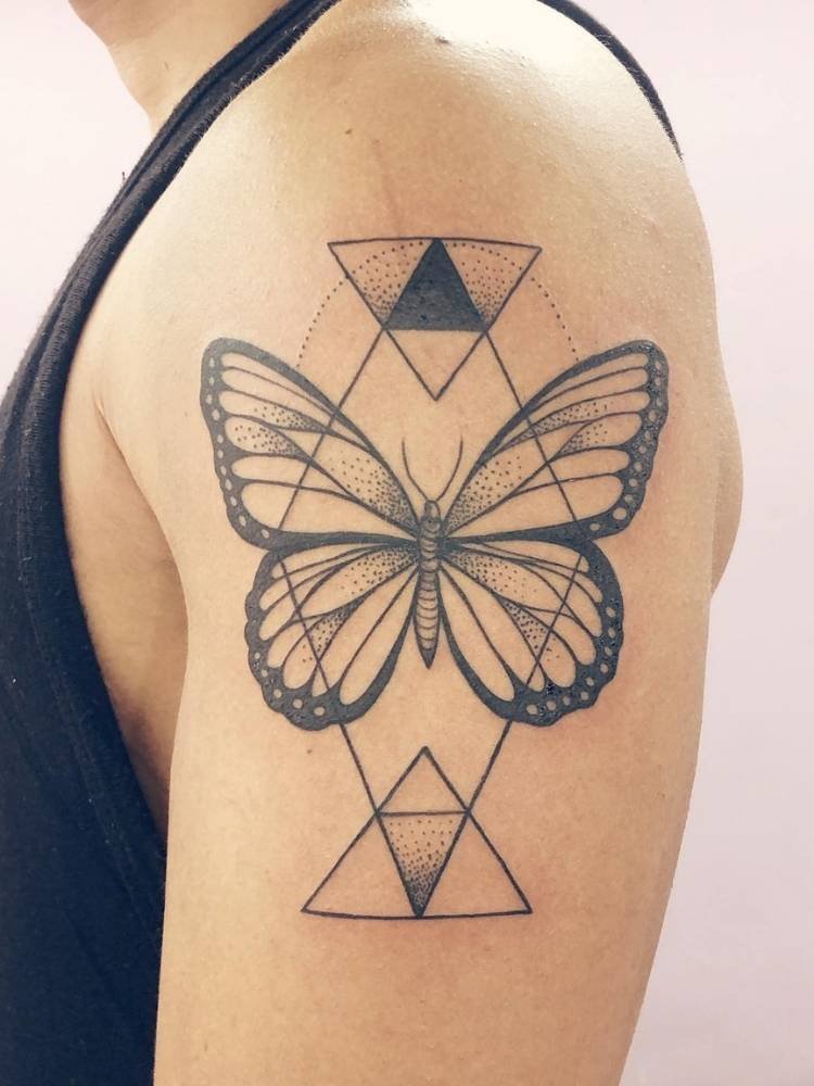 braco-formas-borboleta Tatuagem de borboleta com traços finos e grossos no bíceps de homem de pele clara. Ela acompanha diversos traços triangulares.
