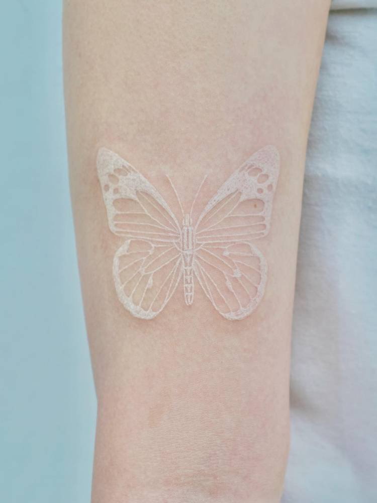 branco-traco-borboleta Tatuagem de borboleta com traços finos e um pouco mais grossos na cor branca. Foi feita no braço de uma pessoa de pele clara.