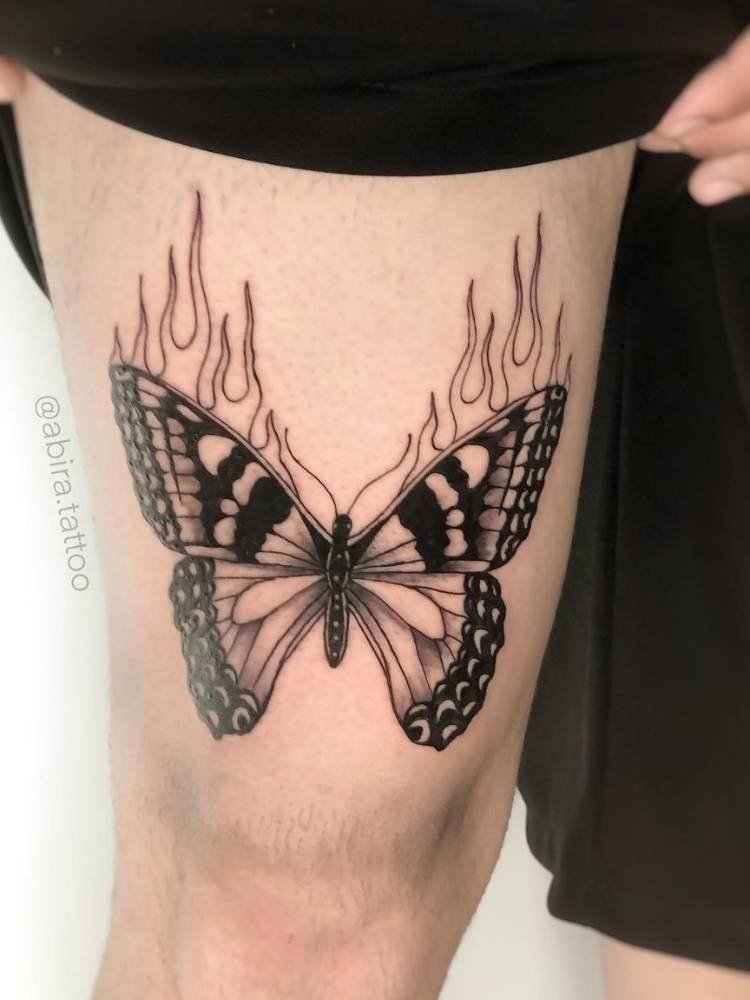 coxa-borboleta-fogo Tatuagem grande de borboleta na coxa de pele clara com sombreamento, traços grossos e detalhes de chamas.