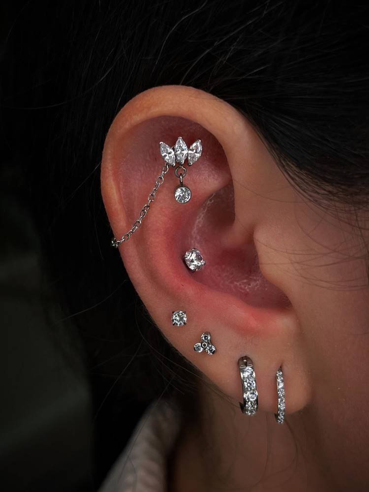 Orelha com piercing na scapha, conch e quatro brincos no lóbulo, sendo um ponto de lux, uma flor e suas argolas