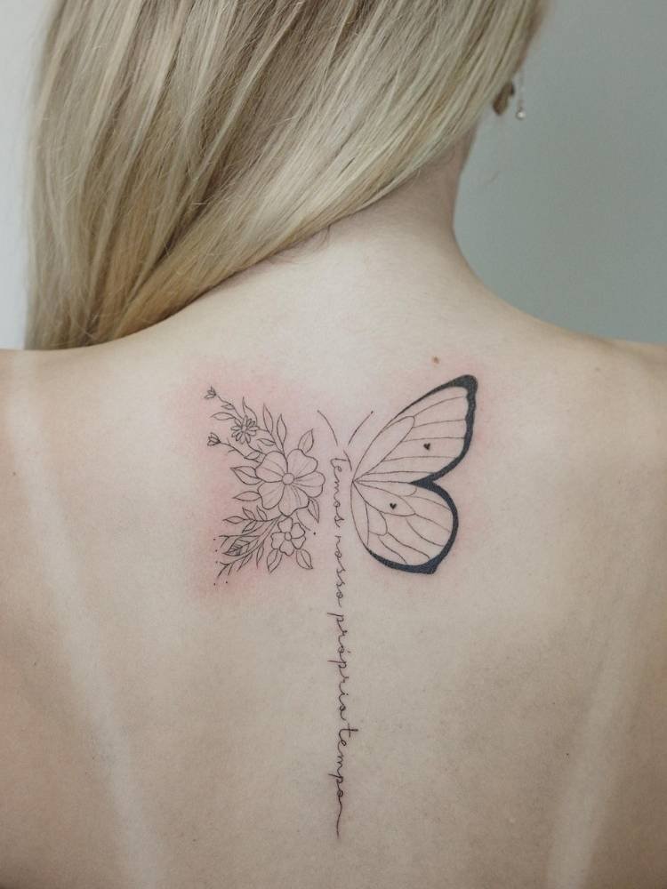 flor-frase-borboleta-costas Tatuagem de borboleta com metade da asa em traços finos e grossos. A outra metade da asa é comporta por flores. O corpo do inseto é uma frase que se estende na coluna: "temos nosso prórpio tempo". Ela foi feita nas costas de uma mulher loira de pele clara.