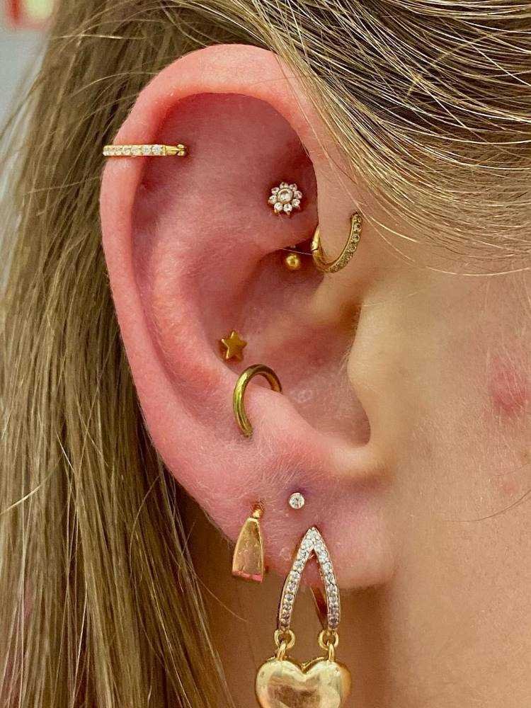 Orelha com piercings em dourado na helix, rook, anti hélix, snug e conch, além de três furos no lóbulo.