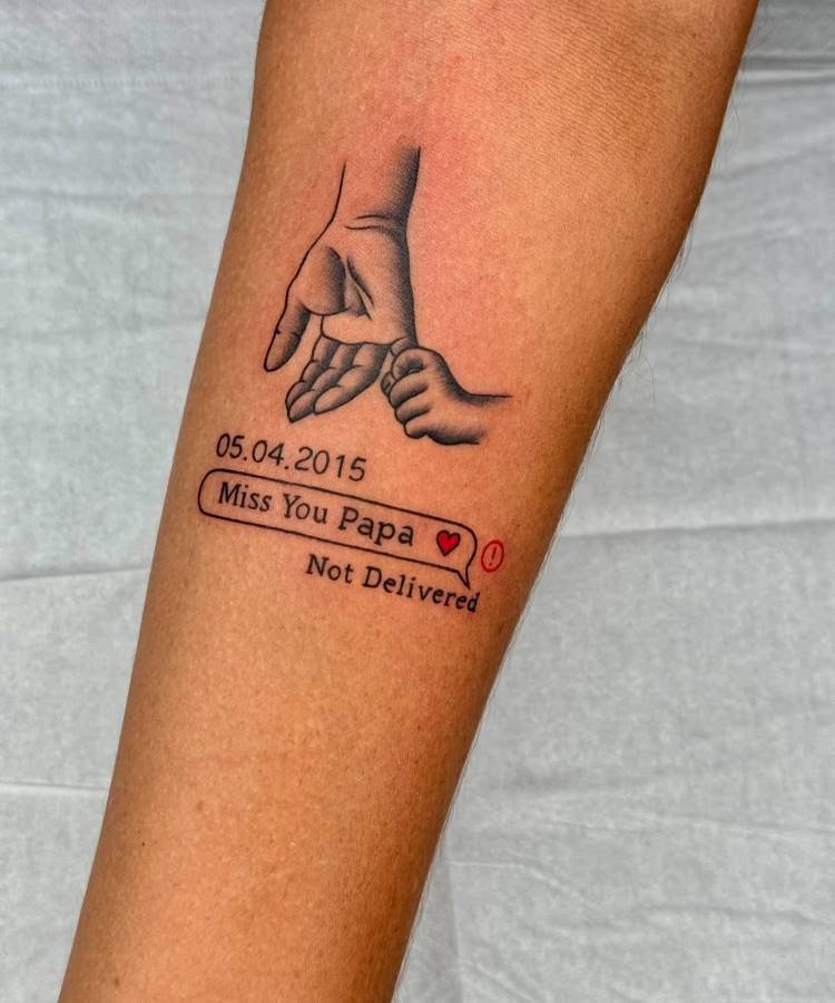 mae-pai-tatuagem-12 A imagem exibe uma tatuagem no antebraço de uma pessoa, apresentando uma mão adulta segurando a mão de uma criança. Abaixo, há a data "05.04.2015" e uma caixa de diálogo de mensagem com "Miss You Papa ❤️🩹" e "Not Delivered" em texto menor. A tatuagem é em preto e cinza.