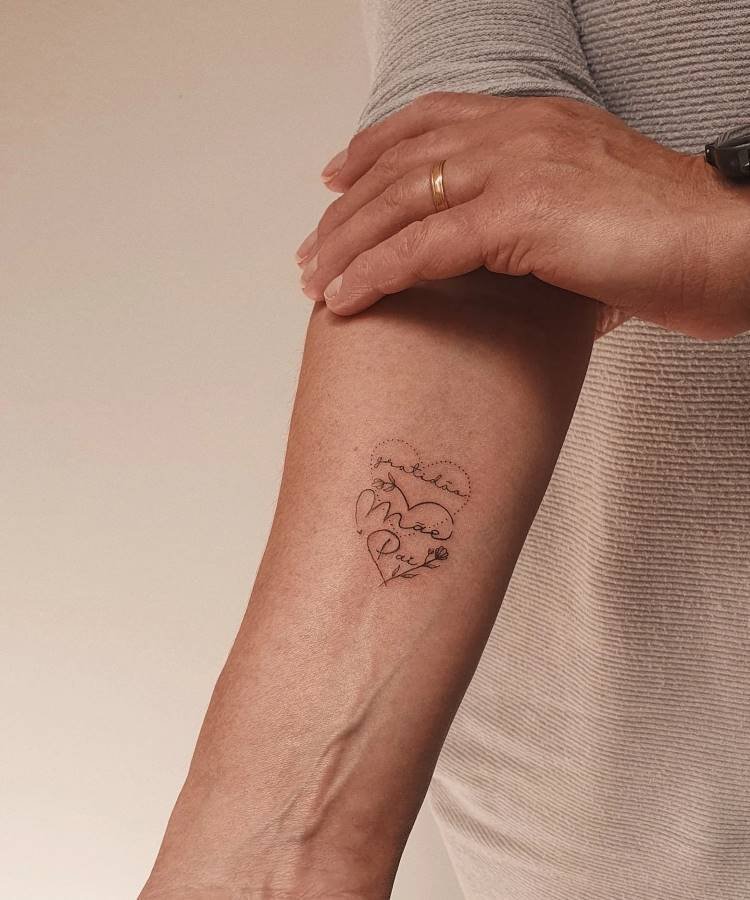 mae-pai-tatuagem-14 A imagem exibe uma tatuagem no antebraço de uma pessoa, representando um coração formado por uma linha pontilhada. Dentro dele, as palavras "gratidão", "Mãe" e "Pai" estão escritas em caligrafia delicada. Um anel dourado é visível na mão da pessoa, que veste uma camisa listrada.A imagem exibe uma tatuagem no antebraço de uma pessoa, representando um coração formado por uma linha pontilhada. Dentro dele, as palavras "gratidão", "Mãe" e "Pai" estão escritas em caligrafia delicada. Um anel dourado é visível na mão da pessoa, que veste uma camisa listrada.
