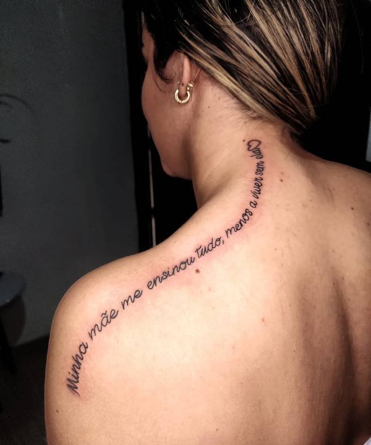 Uma tatuagem em espiral no ombro e pescoço de uma mulher diz: "Minha mãe me ensinou tudo, menos a viver sem ela ❤️". O cabelo está preso e há um brinco de argola dourado. A pele está clara e a tatuagem é bem visível.