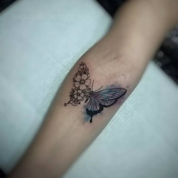 metade-colorida-metade-flor-borboleta Tatuagem de borboleta no braço de uma mulher de pele clara sendo metade da asa em flores de traço fino e a outra metade uma asa em estilo aquarela em azul.