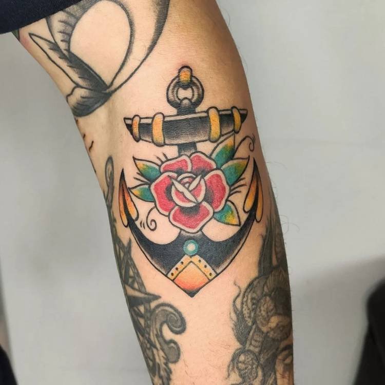 Pessoa de pele clara com tatuagem old school de âncora com flor colorida