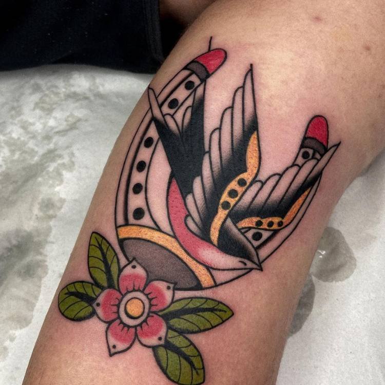 Pessoa de pele clara com tatuagem de andorinha, ferradura e flores coloridas e old schoool