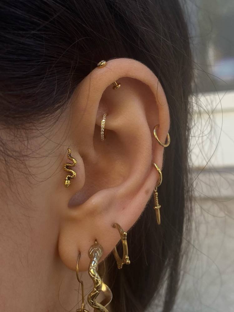 Projeto auricular em dourado com piercing no rook, cobra no tragus, argola no hélix e lóbulo.