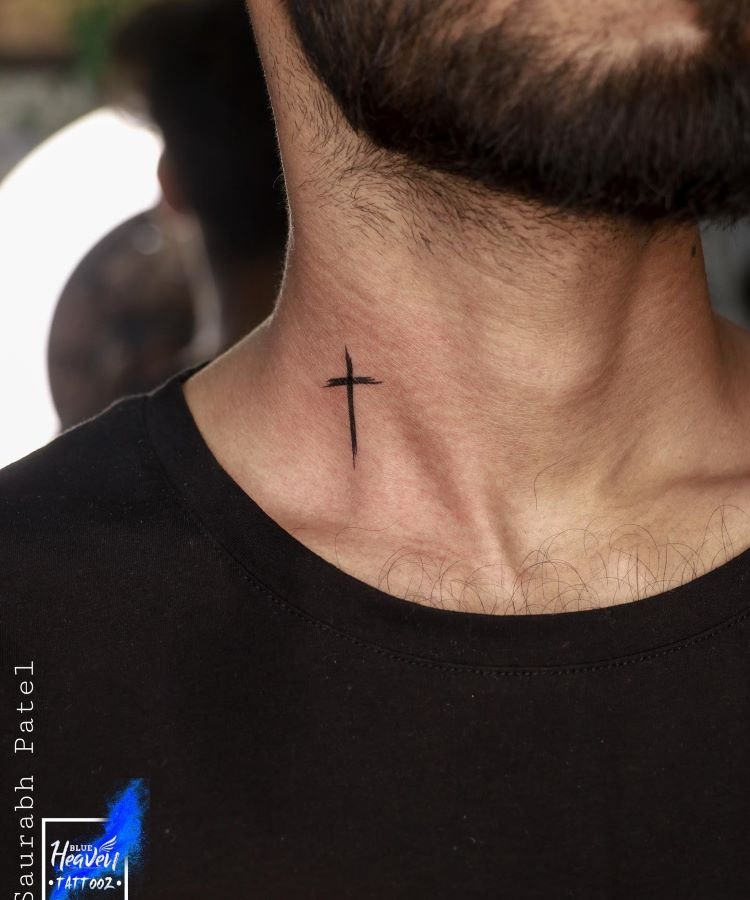 tatuagem-de-cruz-no-pescoco-10-1 A imagem mostra uma pessoa com barba curta e cabelo escuro, usando uma camiseta preta. Ela tem uma tatuagem no pescoço de uma cruz simples e preta, localizada na parte frontal do pescoço, logo abaixo da linha do queixo. A tatuagem é minimalista e centralizada.
