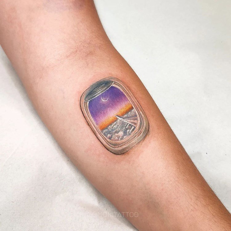 Tatuagem de viagem no braço de janela de avião com vista para a asa e um céu sobre as nuvens