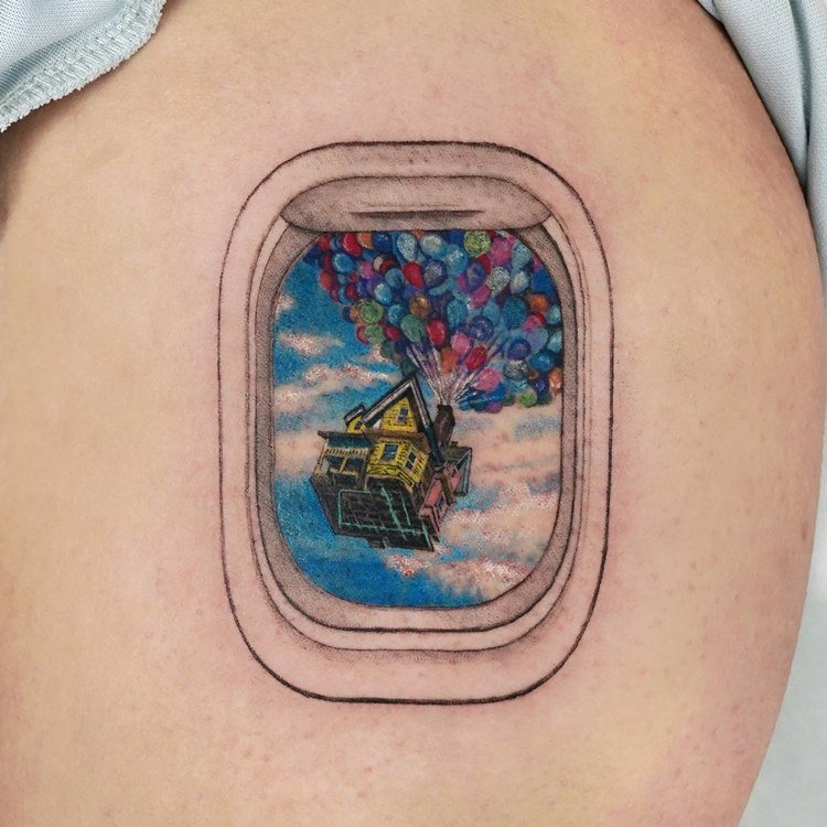 Tatuagem de viagem no braço de janela de avião com vista para céu com casa voando com balões do filme UP em Altas Maravilhas