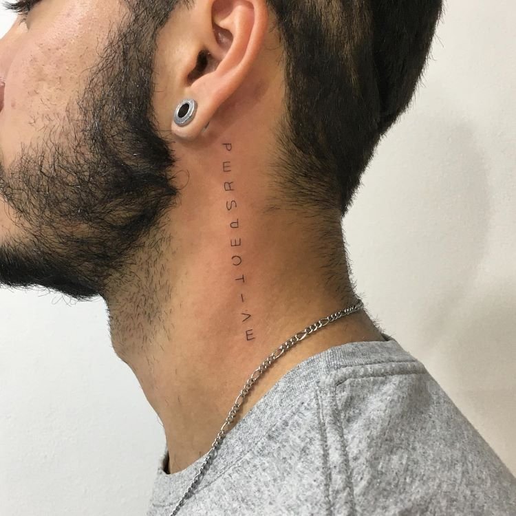 tatuagem-escrita-no-pescoco-3-1 A imagem mostra uma pessoa de perfil com barba e cabelo curto. Ela tem uma tatuagem no pescoço com a palavra "PERSPECTIVE" escrita verticalmente em letras finas. A pessoa usa um alargador na orelha e uma corrente prateada.