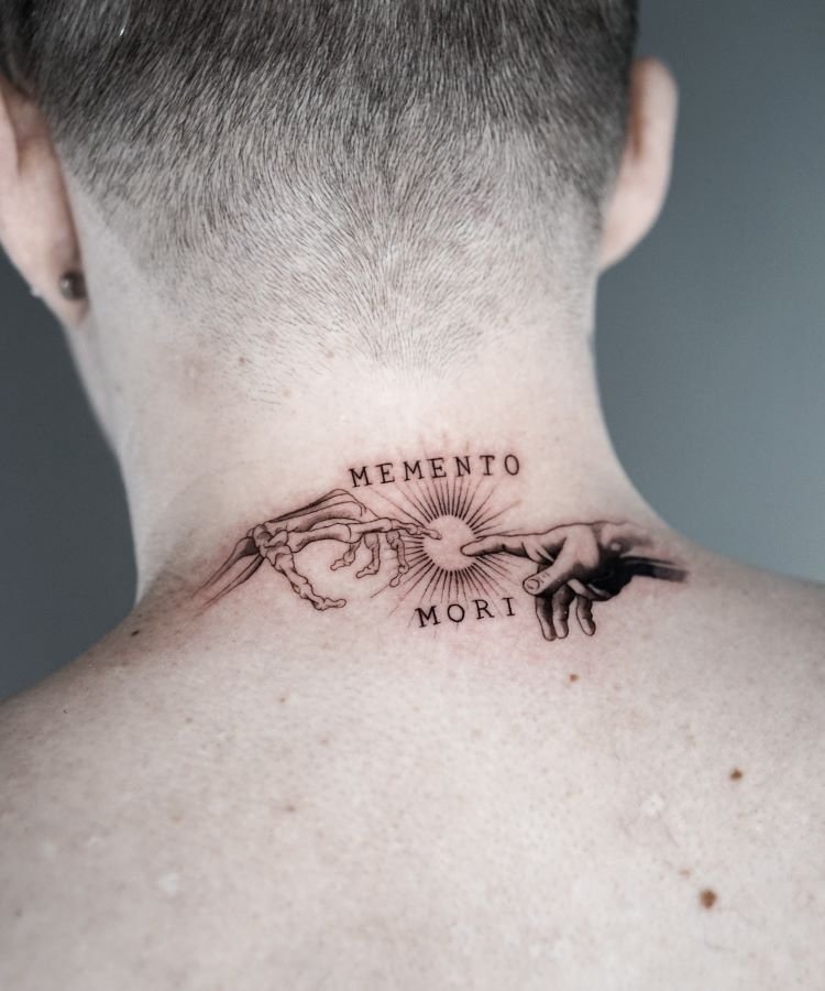 tatuagem-escrita-no-pescoco-6-1 A imagem mostra uma pessoa de costas com cabelo curto. Ela tem uma tatuagem no pescoço que representa duas mãos se tocando, uma esqueleto e outra humana, com as palavras "Memento Mori" acima e abaixo. A tatuagem é detalhada em preto e ocupa a parte superior das costas.