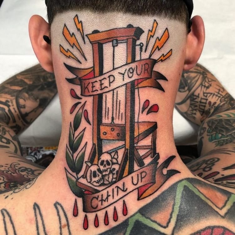 tatuagem-escrita-no-pescoco-8-1 A imagem mostra uma pessoa de costas com cabelo curto. Ela tem uma tatuagem no pescoço de uma guilhotina com as palavras "Keep Your Chin Up" escritas em uma faixa. A tatuagem é colorida e detalhada, cobrindo a parte de trás do pescoço e parte das costas.