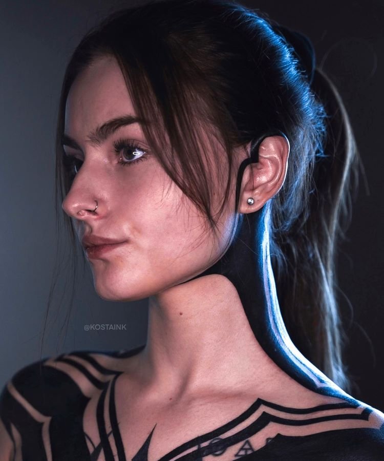 tatuagem-feminina-no-pescoco-12-1 A imagem mostra uma pessoa de perfil com cabelo castanho preso em um rabo de cavalo. Ela tem uma tatuagem no pescoço que é uma faixa preta que se estende até o ombro. A pessoa usa um piercing no nariz e um brinco pequeno na orelha.