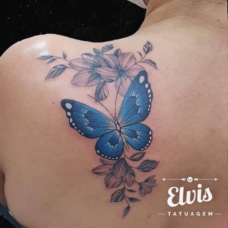 tatuagem-feminina-ombro-borboleta-azul-flores Mulher de pele clara de costas com tatuagem grande de borboleta azul com várias flores em preto