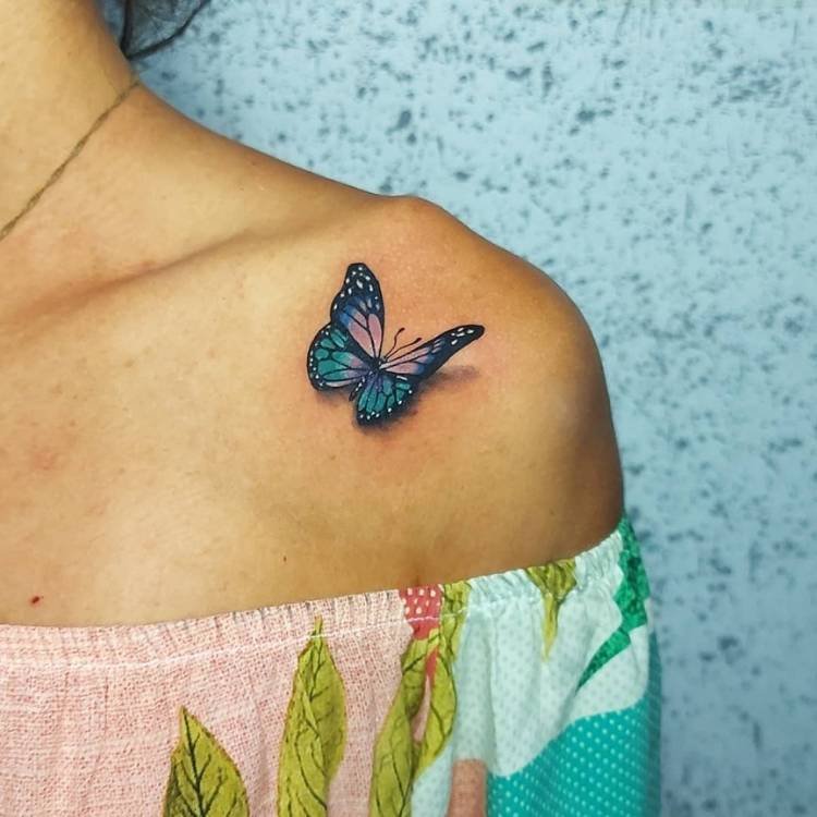 tatuagem-feminina-ombro-borboleta-azul-sombra Mulher de pele clara usando blusa de ombro a ombro colorida e tendo tatuagem de borboleta azul sombreada no ombro