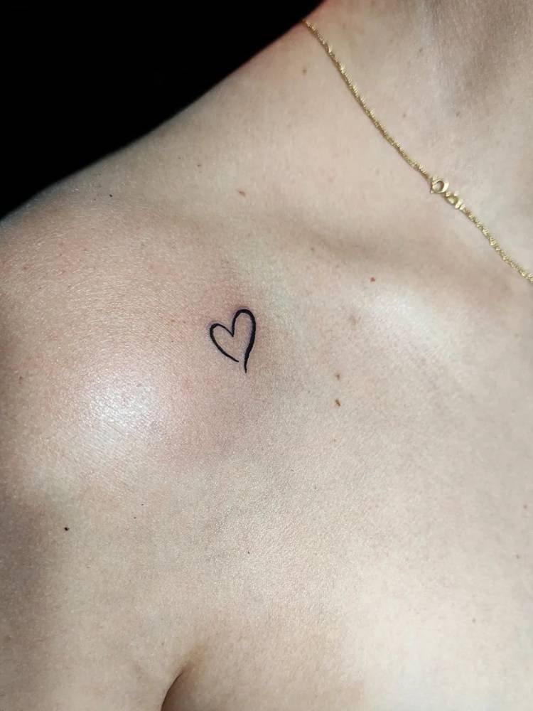 tatuagem-feminina-ombro-corntono-coracao Mulher de pele clara com corrente de dourada e contorno grosso de coração tatuado no ombro