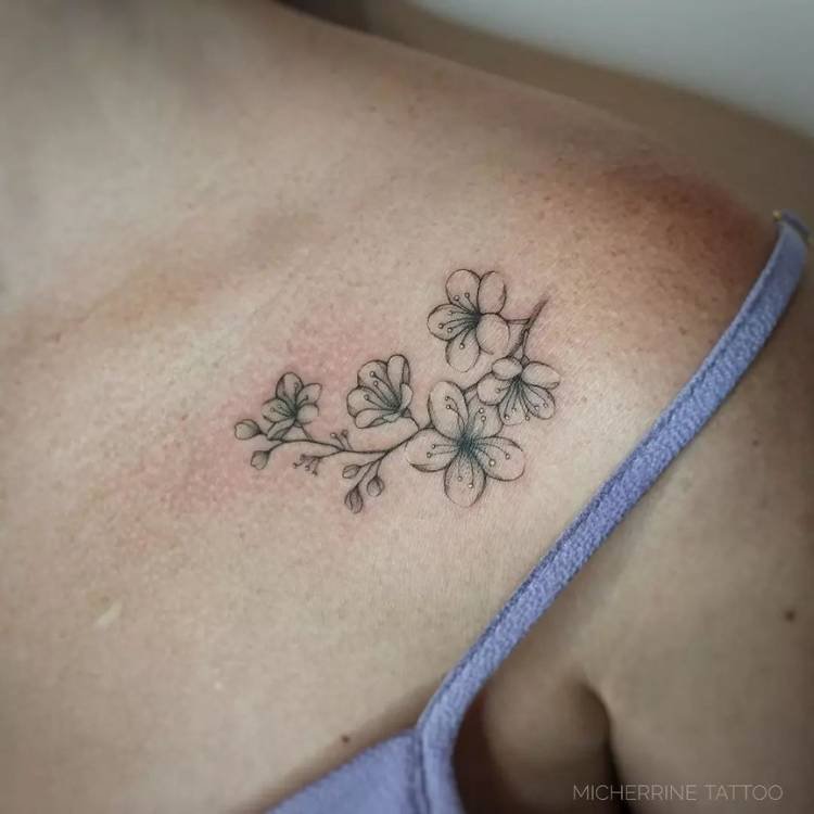 tatuagem-feminina-ombro-delicada-flor Mulher de pele clara com regata cinza e tatuagem de ramo de flores em fine line com detalhes em amarelo claro