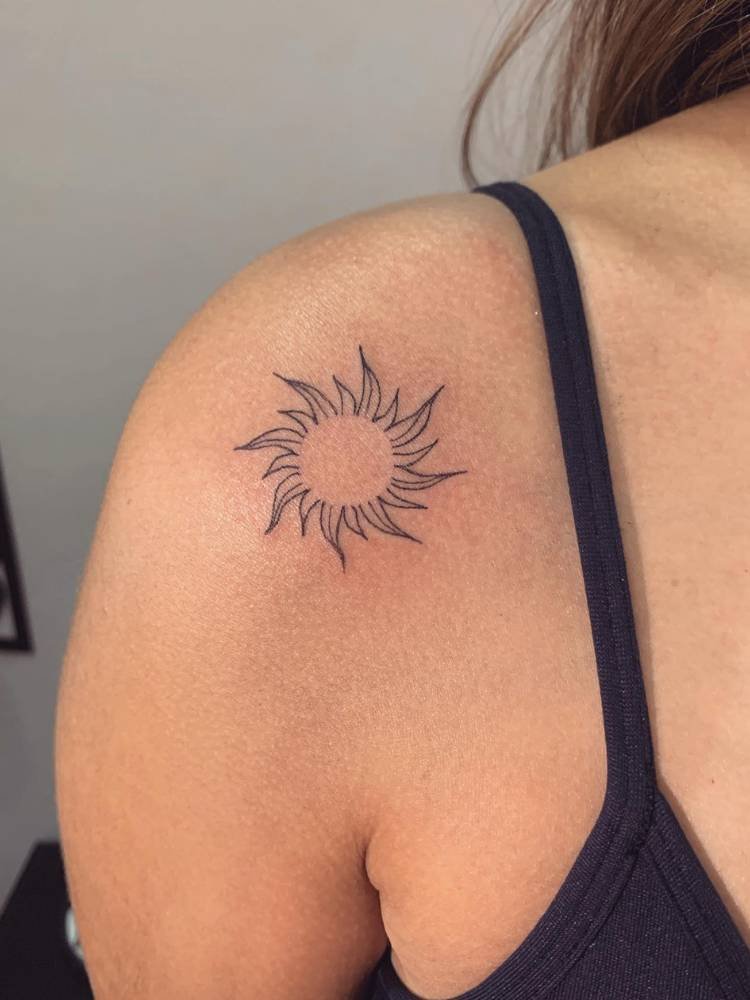 tatuagem-feminina-ombro-sol-3 Mulher de pele clara usando regata preta e com tatuagem fine line no ombro, do sol estilo Enrolados