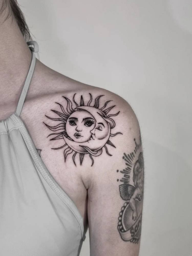 tatuagem-feminina-ombro-sol-lua Mulher de pele clara usando blusa verde e com tatuagem de sol e lua em preto e traços grossos no ombro estilo black work