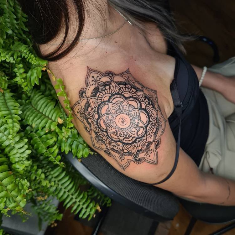 tatuagem-feminina-ombro-sombra-mandala Mulher de pele clara usando corset preto e calça jeans, com uma tatuagem de mandala sombreada no ombro