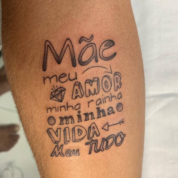 tatuagem-mae-pai-4 A imagem apresenta uma tatuagem no antebraço de uma pessoa com a palavra "Mãe" destacada. Abaixo, frases como "meu AMOR", "minha rainha", "minha VIDA" e "Meu TUDO" são escritas com diferentes fontes e alguns símbolos, como um diamante e setas. A tatuagem é em preto.