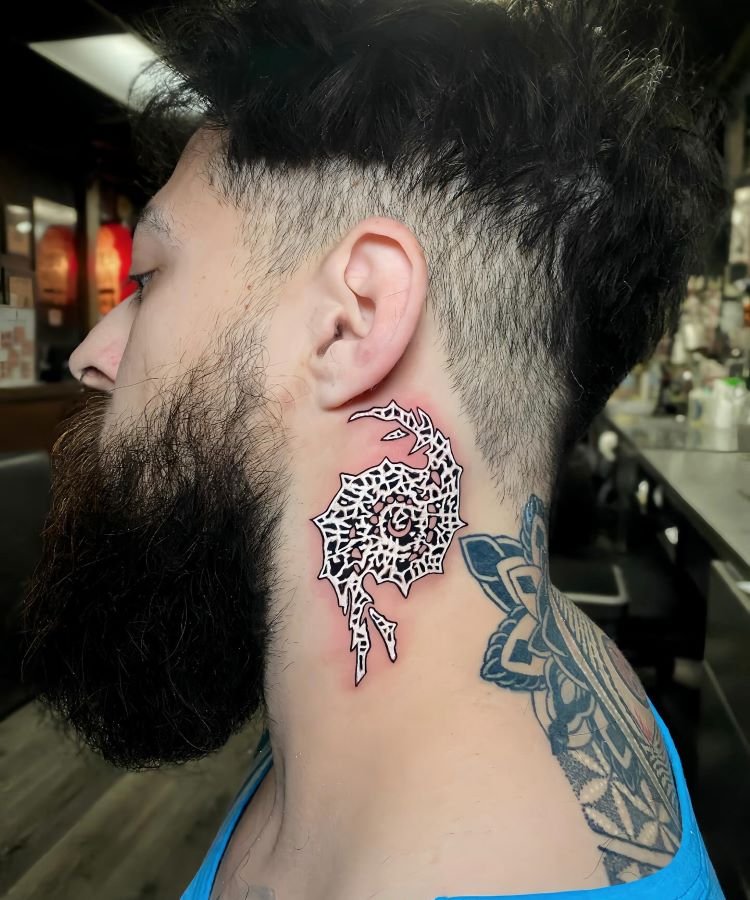 tatuagem-masculina-no-pescoco-16 A imagem mostra uma pessoa de perfil com cabelo curto e barba. Ela tem uma tatuagem no pescoço de um design abstrato em preto e vermelho, parecendo um padrão tribal. A pessoa também tem uma tatuagem geométrica no ombro, visível pela camiseta azul cavada.
