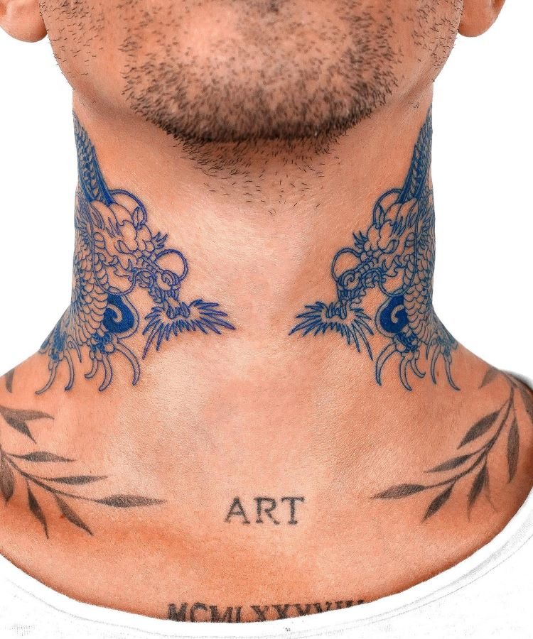 tatuagem-masculina-no-pescoco-23 A imagem mostra uma pessoa com uma tatuagem no pescoço de dois dragões azuis, um de cada lado, cujas cabeças se encontram na frente. A pessoa tem barba rala e a palavra "ART" tatuada na parte inferior do pescoço.