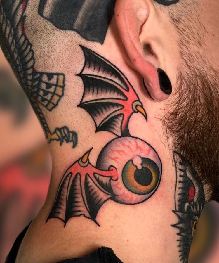 tatuagem-masculina-no-pescoco-4 A imagem mostra uma pessoa de perfil com barba e alargador preto na orelha. Ela tem uma tatuagem no pescoço de um olho com asas de morcego em estilo de desenho animado, com cores vivas como vermelho, preto e amarelo. A tatuagem está localizada na lateral do pescoço.