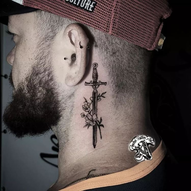 tatuagem-masculina-pescoco-7-1 A imagem mostra uma pessoa de perfil usando um boné vermelho e preto. Ela tem uma tatuagem no pescoço de uma espada vertical cercada por flores. A pessoa tem barba e usa vários piercings na orelha.