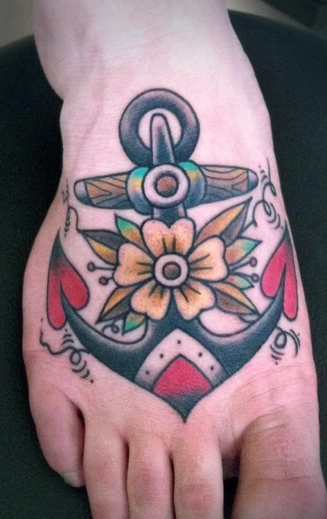 Pessoa de pele clara com tatuagem de âncora old school colorida no pé