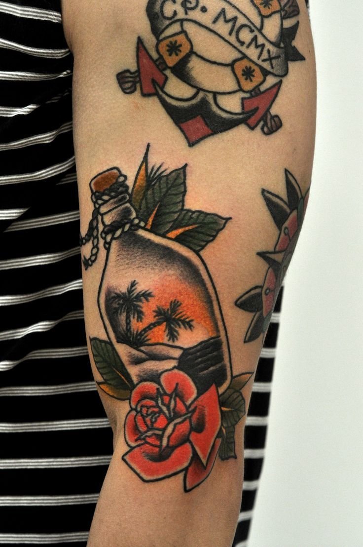 Âncora e garrafa com paisagem marítima tatuadas em estilo old school, ambas com flores