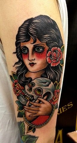 Tatuagem Old School de cigana com cabelo preto, flor vermelha, e segurando uma caveira branca