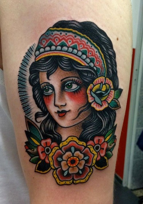 Tatuagem Old School de cigana com flor no cabelo preto e três flores coloridas abaixo
